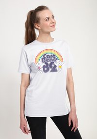 Bílý tričko s barevným duhovým designem a grafikou Medvídků Care Bears, vyrobené z bavlny, s volným střihem a krátkými rukávy.