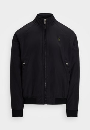 Veste noire zippée avec poignets et ourlet côtelés, deux poches latérales zippées et petit logo vert brodé sur la poitrine gauche.