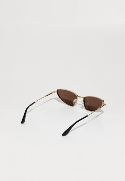 Ochelari de soare eleganți, cu ramă metalică aurie, lentile de culoare maro și vârfuri curbate din plastic negru, așezati pe o suprafață albă.