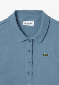 Slim fit ribbad polo-shirt i ljusblått med treknapps knäppning, liten grön broderad krokodil-logotyp och textilstruktur.