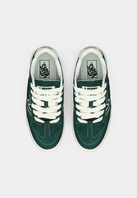 Grüne Wildleder-Sneaker mit weißen Schnürsenkeln, einer gepolsterten Zunge und einer strukturierten Außensohle. Merkmale sind Nahtakzente und das Markenlogo auf der Zunge.