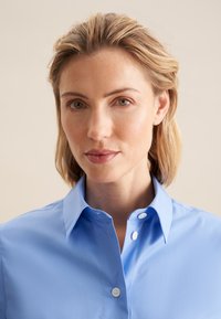 Jasnoniebieska koszula z guzikami, o usztywnionym kołnierzyku, gładkiej fakturze i dwóch przednich guzikach. Minimalistyczny design, odpowiednia na różne okazje.