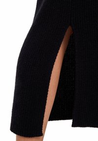 Schwarzer gerippter Strickrock mit seitlichem Schlitz, der die darunterliegende Haut zeigt, bis zur Mitte geschnitten, um sich auf den Schlitzbereich zu konzentrieren.