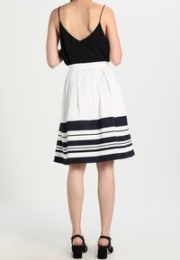 Top noir à bretelles et jupe blanche avec des rayures horizontales navy ; la jupe est plissée et tombe juste en dessous du genou.