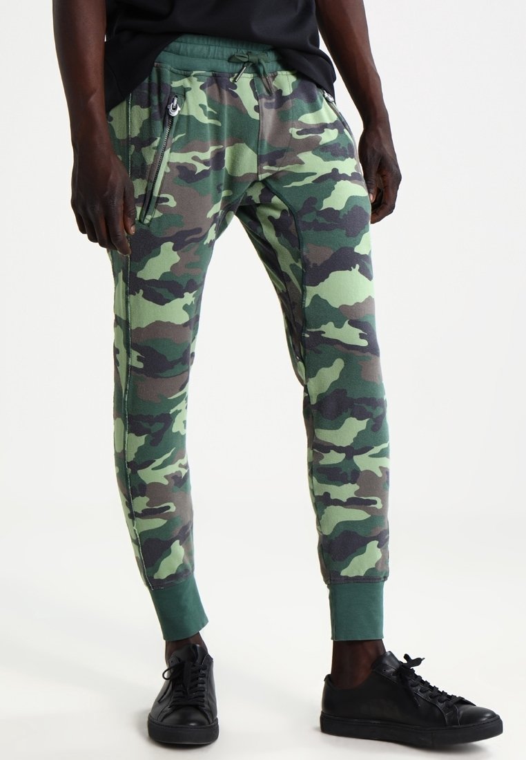 Kamouflagebyxor i gröna och bruna nyanser, med smal passform, snörning i midjan, blixtlåsfickor på sidorna och ribbade ärmslut.