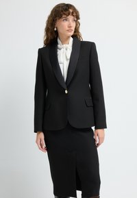 Černý blazer se saténovými klopami, jedno zlaté tlačítko a dvě přední kapsy. V kombinaci s černou tužkovou sukní s bočním rozparkem.