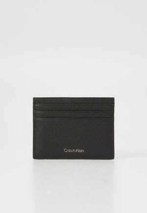 Porte-carte en cuir noir avec trois fentes pour cartes et logo Calvin Klein en argent au centre sur fond blanc.