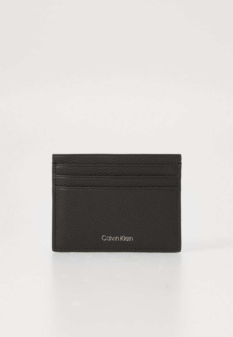 Portofel din piele neagră, cu trei sloturi pentru carduri și logo-ul Calvin Klein în argintiu, situat central pe față, pe un fundal alb.