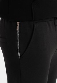 Schwarze Jogginghosen aus weichem Stoff, mit einer Seitentasche mit silbernem Reißverschluss und einem verstellbaren Kordelzugbund.
