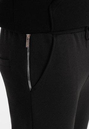 Schwarze Jogginghosen aus weichem Stoff, mit einer Seitentasche mit silbernem Reißverschluss und einem verstellbaren Kordelzugbund.