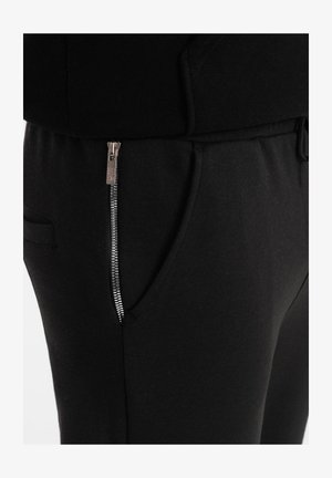 Pantalons de jogging noirs en tissu doux, avec une poche latérale à fermeture éclair argentée et une taille avec cordon de serrage pour un ajustement personnalisé.