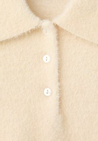 Pullover in lana morbida color crema chiaro, felpato, con colletto a punta e tre piccoli bottoni rotondi al centro della parte anteriore.