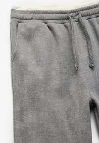 Grå teksturerede sweatpants med et vævet mønster, elastisk talje med snor og sidelommer. Materialet virker blødt og varmt.