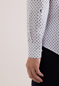 Camicia di cotone con base bianca e pois blu. Il polsino presenta un piccolo dettaglio ricamato e chiusure con bottoni.