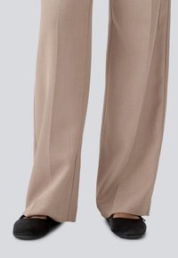 Beige, wide-leg trousers with a smooth, textured fabric. Paired with black, flat shoes featuring rounded toes and subtle accents.