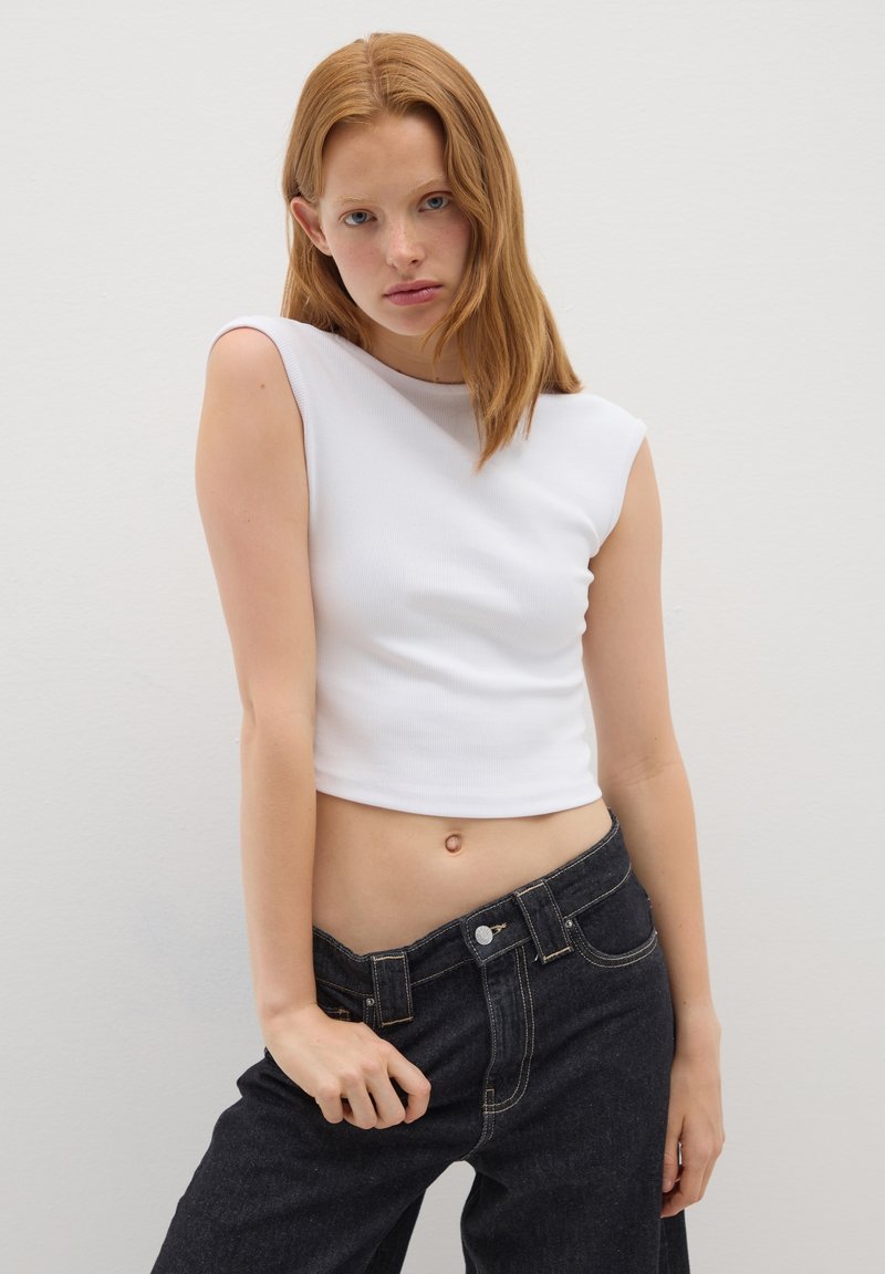 Top corto bianco con texture a coste, vestibilità slim e maniche corte, abbinato a jeans in denim scuro a vita alta con cuciture a contrasto.