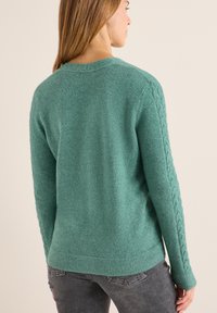 Grüner Strickpullover mit strukturiertem Rücken, geripptem Saum und Zopfmuster-Akzenten an den Ärmeln. Schlichter runder Ausschnitt.