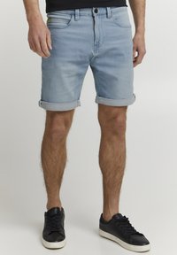 Ljusblå denimshorts med uppvikta benslut, fem fickor och knappstängning. Matchas med svarta snörskor.