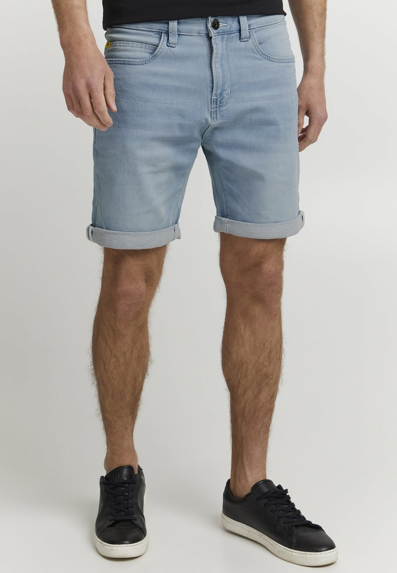 Lys blå denimshorts med oppbrett, fem lommer og knappelukking. Kombinert med svarte snøring sneakers.