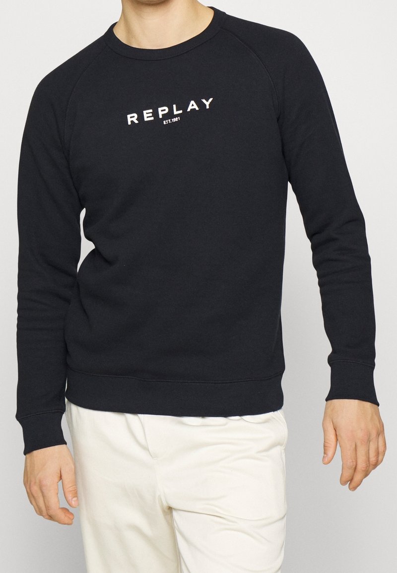 Felpa nera con collo a girocollo, maniche lunghe raglan e logo bianco "REPLAY" sul petto. Tessuto morbido con orlo e polsini a costine.