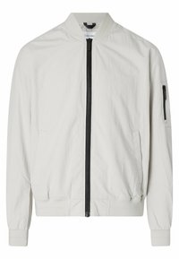 Vaaleanbeige bomber-tyylinen takki, jossa on musta etuvetoketju, resorikaulus, resorit hihansuissa ja helmassa, sivutaskut sekä vetoketjullinen tasku vasemmassa hihaisessa.
