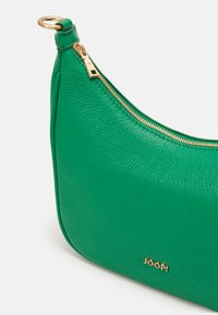 Borsa a spalla verde in pelle con forma curvilinea, zip dorata e dettaglio del marchio sul davanti. La superficie testurizzata aggiunge profondità.