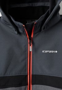 Mørkegrå zip-up jakke med en sort stribe, accentueret af en klar orange lynlås. Har en høj krave og en glat tekstur.