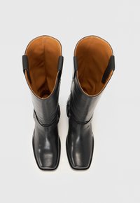 Botas de cuero negro hasta la rodilla con puntera cuadrada, que presentan un acabado liso, interior marrón y dos tiradores laterales para facilitar su colocación.