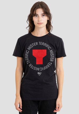 Young woman wearing a black t-shirt with a red geometric logo and "MISTER TERRIFIC" text encircling it on a gray background.