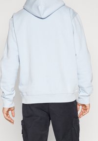 Světle modrá mikina s kapucí z měkkého materiálu, s klokaní kapsou, žebrovanými lemy na rukávech a stahovací šňůrkou na kapuci. Nositelná přes tmavé cargo kalhoty.