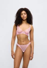 Σετ ροζ εσωρούχων, με σουτιέν διακοσμημένο με δαντέλα και κυματοειδείς άκρες, και ταυτόχρονα ταίριαστο στρινγκ, και τα δύο με διαφανές πουά σχέδιο.