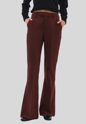 Persona che indossa dei pantaloni flare a vita alta, marrone scuro, con tasche, abbinati a un maglione cropped nero e scarpe nere.