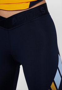Granatowe legginsy sportowe z teksturowanym czarnym pasem, z niebieskimi i żółtymi geometrycznymi wzorami po bokach jako akcent.