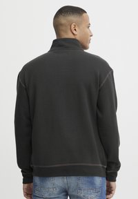 Must must, kõrge kaelusega mustad pullover-sweatid, millel on kontrastsete õmblustega. Kanga välimus on mugav, näidates vabalt liikuvat lõiget ja juhuslikku disaini.