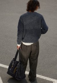 Suéter de punto gris con un ajuste relajado, combinado con pantalones oscuros holgados. Un bolso grande negro presenta herrajes de metal y accesorios de llavero.