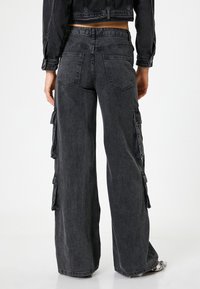 Svarta denim cargobyxor med vida ben, som har sidofickor, en blekt textur och en hög midje-design. Bakifrån visas detaljerad sömnad.