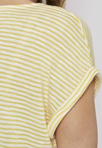 Camiseta a rayas que presenta líneas horizontales alternas en amarillo y blanco, material de algodón suave y mangas cortas enrolladas.
