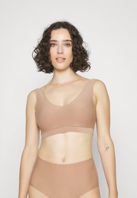 Lichtbruine naadloze bralette met brede bandjes en een v-halslijn, gecombineerd met bijpassende high-waisted slip; gladde stofstructuur.