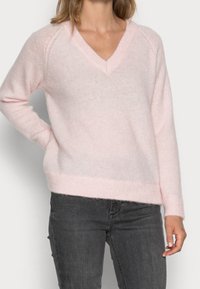 Lyserød v-hals trøje lavet af blødt, fluffet materiale med ribstrikkede manchetter og kant. Har en afslappet pasform og raglanærmer.