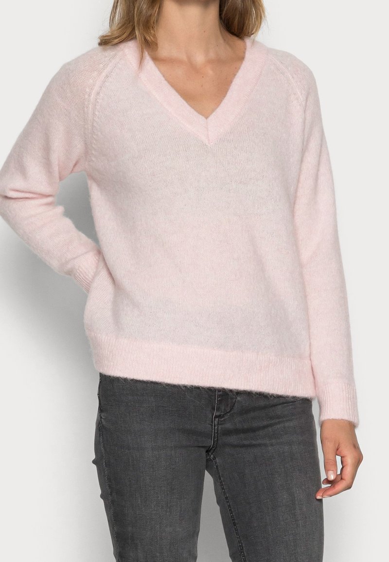 Lyserød v-hals trøje lavet af blødt, fluffet materiale med ribstrikkede manchetter og kant. Har en afslappet pasform og raglanærmer.