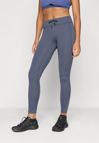 Pelēki sporta legingi, kas izgatavoti no elastīga auduma, ar vidēju vidukļa jostu un sānu šuvēm. Apvienoti ar melniem sporta apaviem.