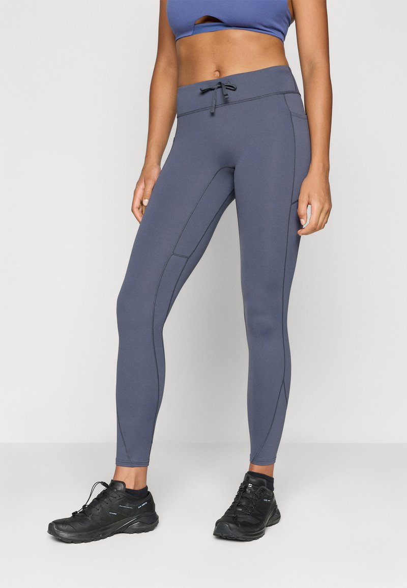 Pelēki sporta legingi, kas izgatavoti no elastīga auduma, ar vidēju vidukļa jostu un sānu šuvēm. Apvienoti ar melniem sporta apaviem.