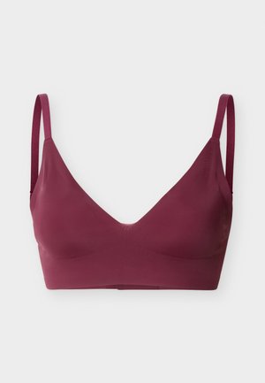 Bezszwowy głęboki bordowy biustonosz typu bralette z cienkimi, regulowanymi ramiączkami i dekoltem w kształcie litery V na jasnym tle.