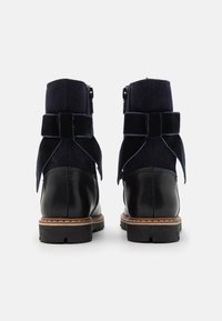 Navy semišové kotníkové boty s koženou špičkou, mašlí vzadu a bočním zipem; texturovaná tkanina a hladký povrch.