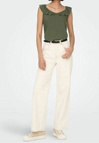 Top senza maniche di un verde oliva con scollatura arricciata, abbinato a jeans a gamba larga color crema a vita alta e sneakers beige. Una cintura nera evidenzia la vita.