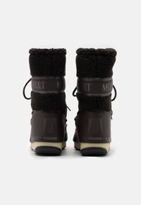 Bottes d'hiver marron foncé avec une tige douce et texturée, doublure en peluche, lacets ajustables et une bande à motifs avec un logo sur les côtés.