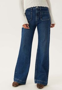 Höga vida jeans i mörkblå denim, med fram- och bakfickor samt knappstängning, kombinerade med en texturerad vit stickad topp.