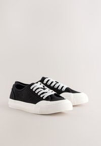 Baskets basses en toile noire avec semelles en caoutchouc blanches et lacets blancs, présentées côte à côte sur un fond neutre.