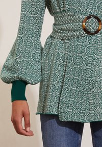 Vihreä kuvioitu paita, joka on valmistettu tekstuurikankaasta ja jossa on pitkät puffihihat, istuva vyötärö pyöreällä ruskealla vyöllä sekä hillitty sivuhalkio.