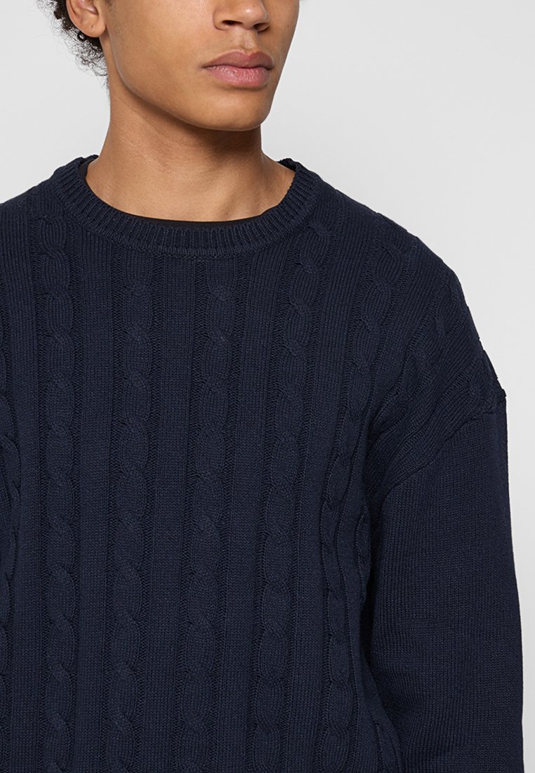Marineblauer Zopfpullover mit Rundhalsausschnitt, gerippten Bündchen und strukturierten Mustern im gesamten Stoff.